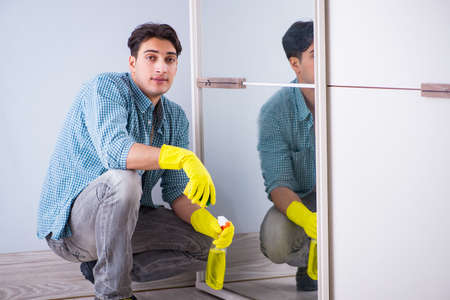 Young man cleaning mirror at hotel roomの写真素材