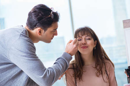 Man doing make-up for cute woman in beauty salon