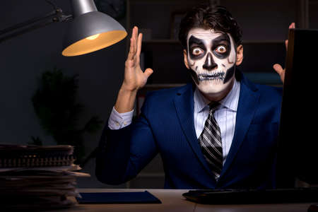 Businessman with scary face mask working late in officeの写真素材