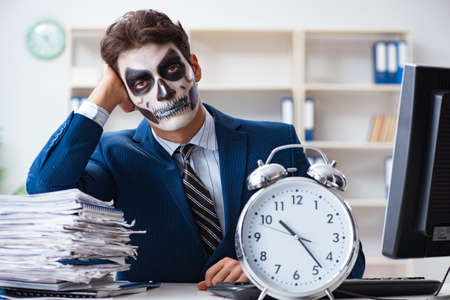 Businessmsn with scary face mask working in officeの写真素材