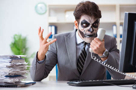 Businessmsn with scary face mask working in officeの写真素材