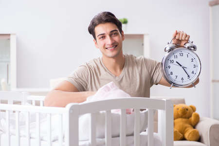 Young dad with clock near newborn baby bed cotの写真素材
