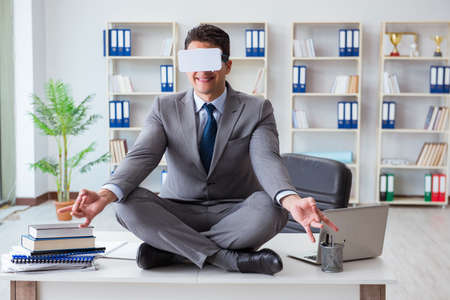 Businessman in virtual reality VR glasses meditating at desk topの写真素材