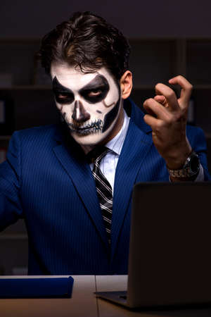 Businessman with scary face mask working late in officeの写真素材