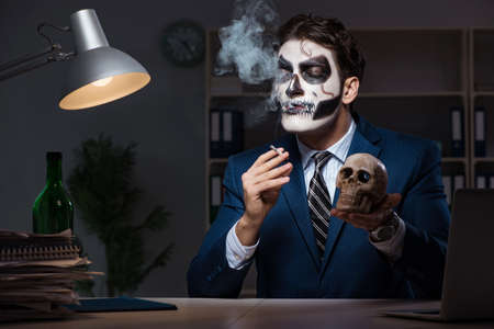 Businessman with scary face mask working late in officeの写真素材