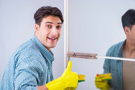 Young man cleaning mirror at home hotelの写真素材