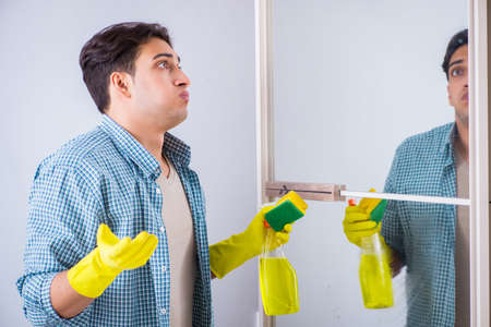 Young man cleaning mirror at home hotelの写真素材
