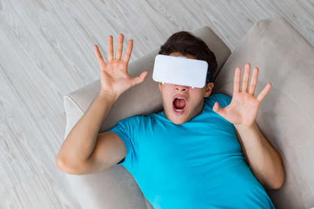 Young man wearing VR glasses relaxing on couch sofaの写真素材