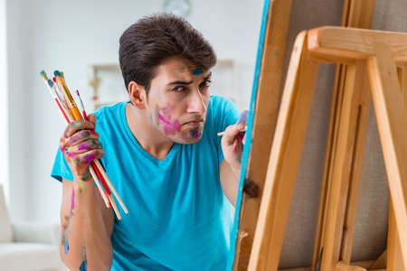 Young funny artist working on new painting in his studio