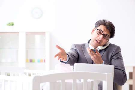 Young businessman trying to work from home caring after newbornの写真素材