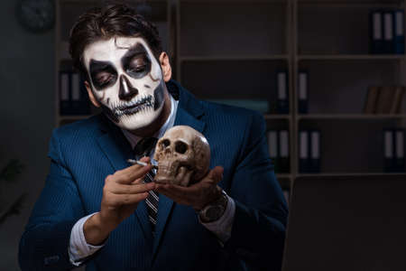 Businessman with scary face mask working late in officeの写真素材