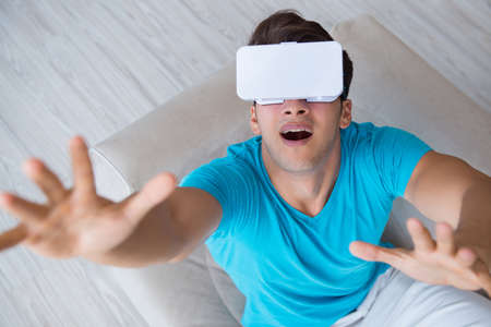Young man wearing VR glasses relaxing on couch sofaの写真素材