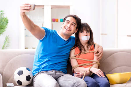 Man tying up his wife to watch sports footballの写真素材