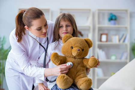 Woman female doctor examining little cute girl with toy bearの写真素材