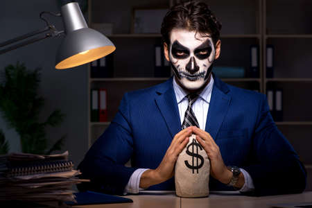 Businessman with scary face mask working late in officeの写真素材