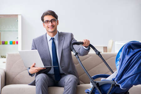 Businessman looking after newborn baby at home and teleworkingの写真素材