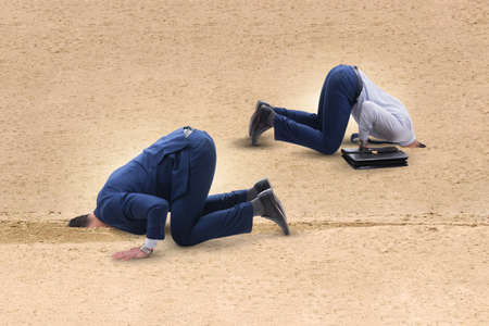 Businessman hiding his head in sand escaping from problemsの写真素材