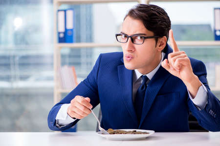 Funny businessman eating gold coins in officeの写真素材