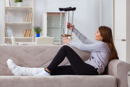 Young woman with broken leg at homeの写真素材