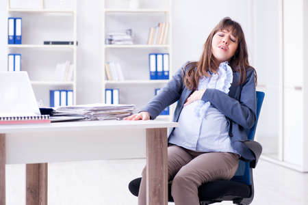 Pregnant woman struggling to do work in officeの写真素材