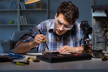 Young repair technician soldering electrical parts on motherboar
