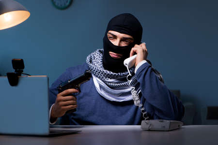 Terrorist burglar with gun working at computer