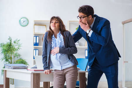 Pregnant woman struggling in the office and getting colleague heの写真素材