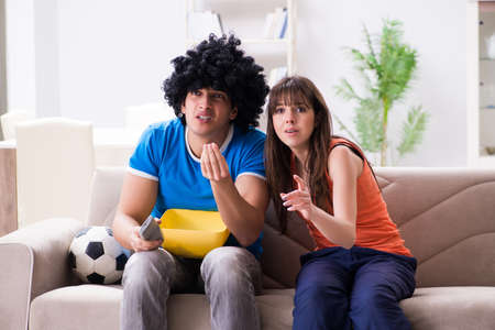 Young man watching football with his wife at homeの写真素材