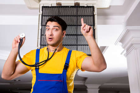 Repairman repairing ceiling air conditioning unitの写真素材