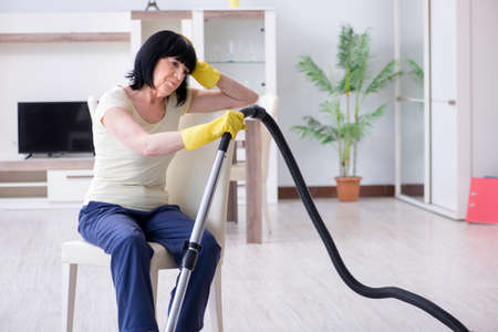 Senior old woman tired after vacuum cleaning houseの写真素材