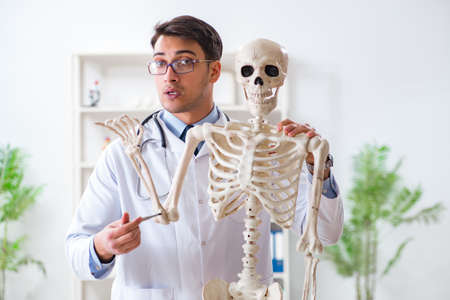 Yong male doctor with skeleton isolated on white