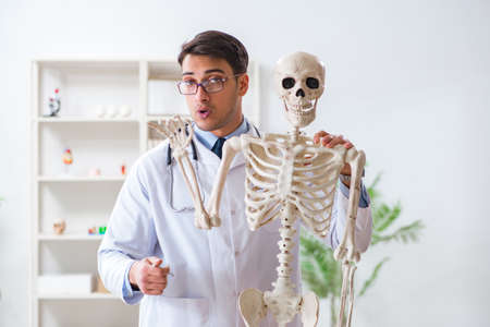 Yong male doctor with skeleton isolated on white