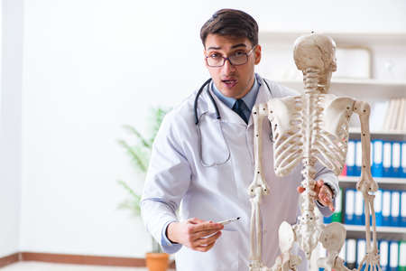 Yong male doctor with skeleton isolated on white