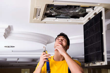 Repairman repairing ceiling air conditioning unitの写真素材