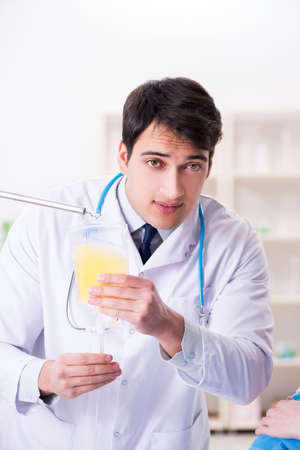 Young male doctor with bag of blood plasma in hospitalの写真素材