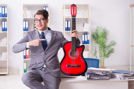 Young handsome businessman playing guitar in the officeの写真素材