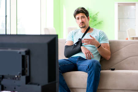 Arm injured man sitting on the sofa watching tv