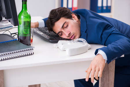 Young businessman employee drinking in the office at deskの写真素材