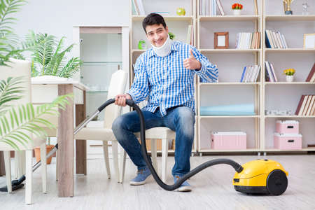 Injured man with neck injury vacuum cleaning houseの写真素材