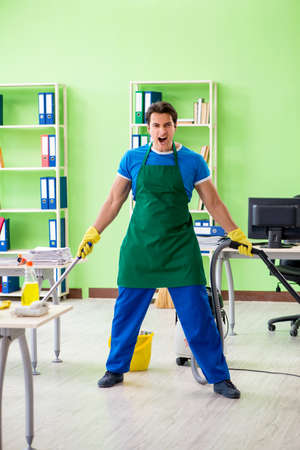 Handsome man cleaning office with vacuum cleanerの写真素材
