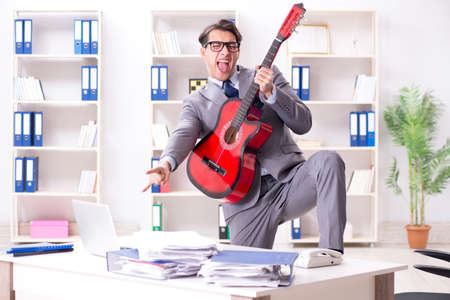 Young handsome businessman playing guitar in the officeの写真素材
