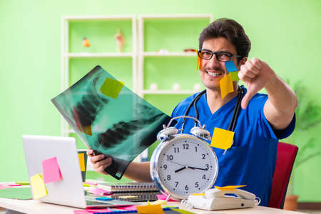 Young doctor sitting in hospital with many conflicting prioritie