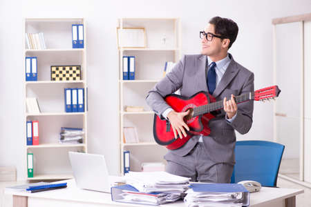 Young handsome businessman playing guitar in the officeの写真素材