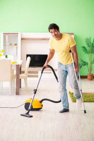 Injured man on crutches vacuum cleaning houseの写真素材