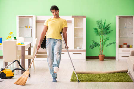 Injured man on crutches cleaning houseの写真素材