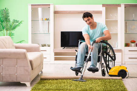 Disabled man on wheelchair vacuum cleaning houseの写真素材