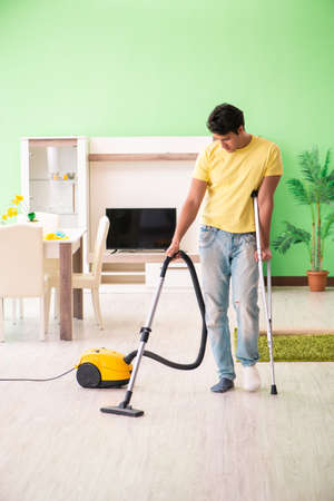 Injured man on crutches vacuum cleaning houseの写真素材