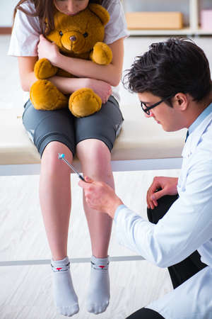 Doctor checking up young girls reflexes with hammerの写真素材