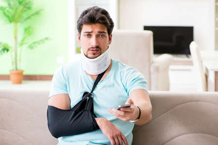Young student man with neck and hand injury sitting on the sofa
