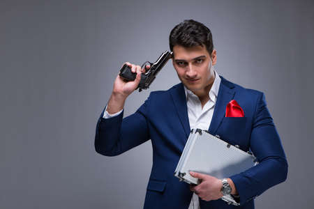Handsome man holding a gun against gray backgroundの写真素材